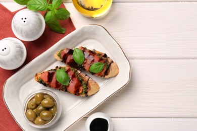 Delicious bruschettas with balsamic vinegar and toppings served with olives on white wooden table, flat lay. Space for text