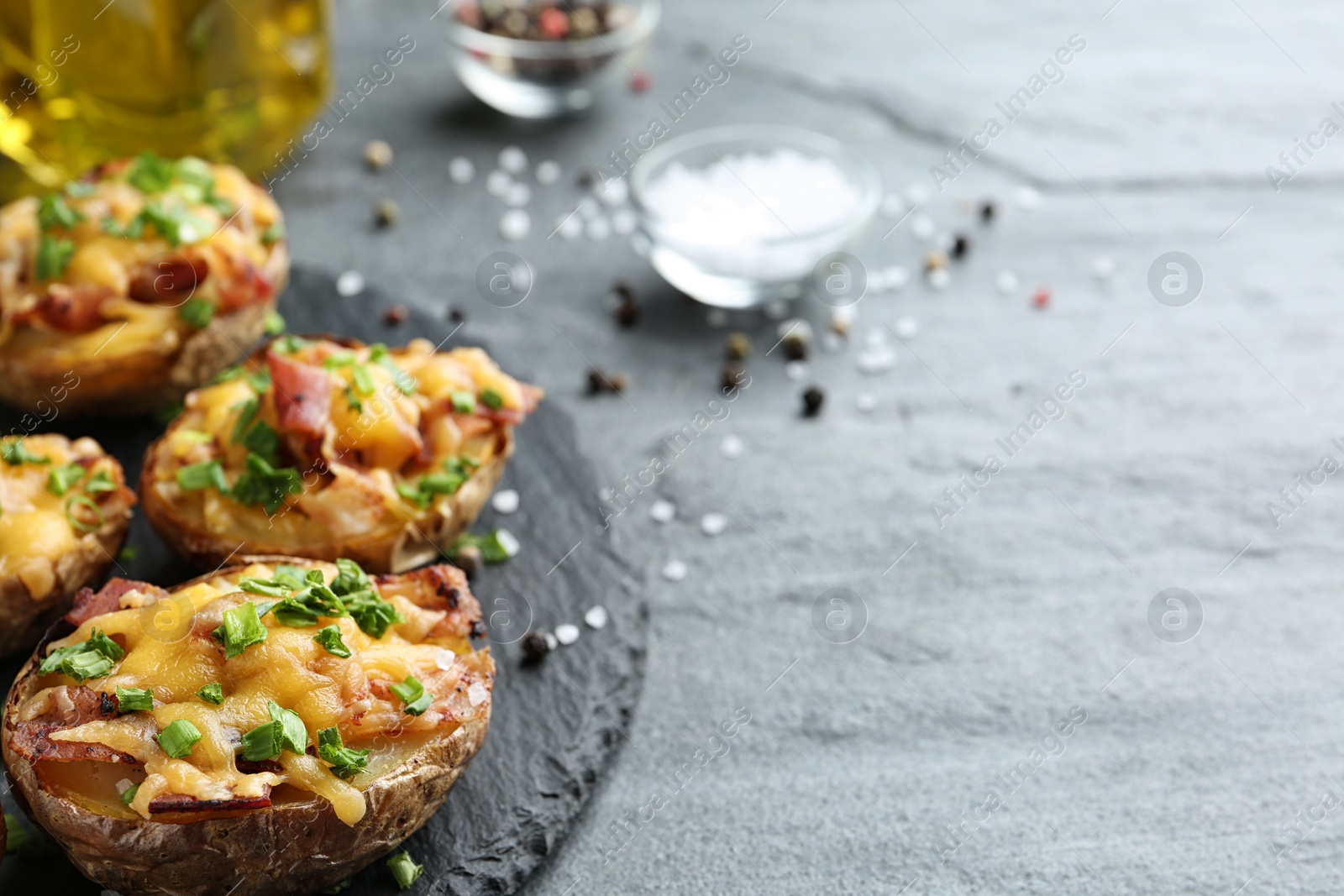 Photo of Slate plate with baked potatoes on table, closeup. Space for text