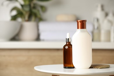 Bottle of shampoo, hair oil and wooden comb on white table in bathroom, space for text