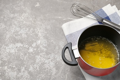 Pot of melting butter and whisk on grey table. Space for text