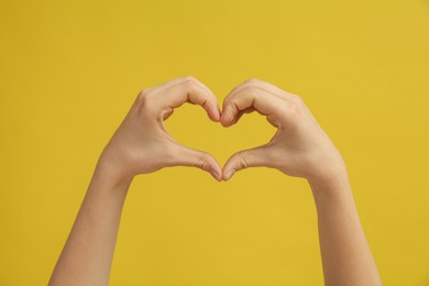 Woman making heart with fingers on yellow background, closeup