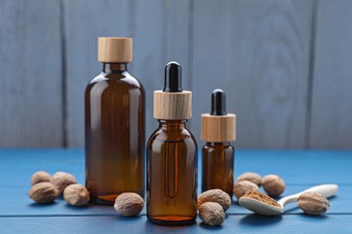 Bottles of nutmeg oil and nuts on blue wooden table