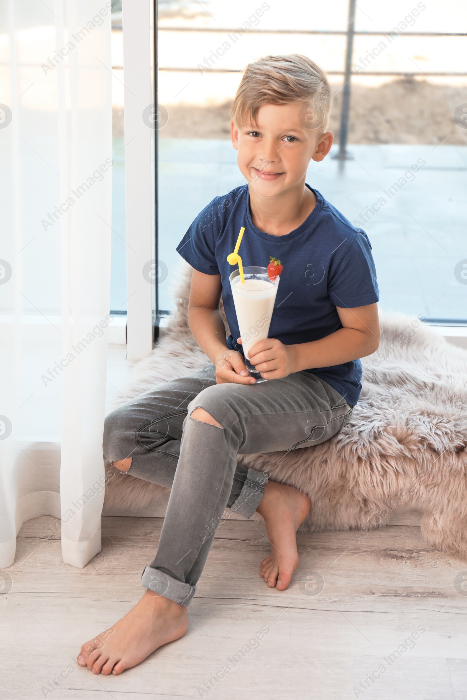 Photo of Little boy with glass of milk shake near window indoors