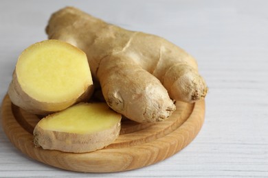 Photo of Cut and whole fresh ginger on white wooden table, closeup