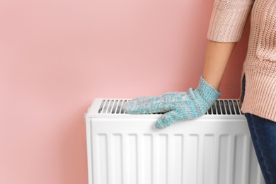 Woman in glove warming hand on heating radiator near color wall. Space for text