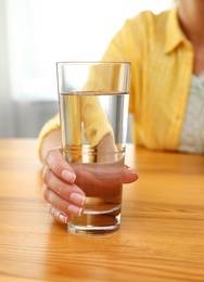 Photo of Woman holding glass of water at wooden table, closeup. Refreshing drink
