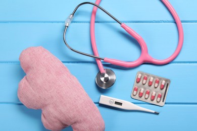 Photo of Pillow, stethoscope, thermometer and pills on light blue wooden background, flat lay