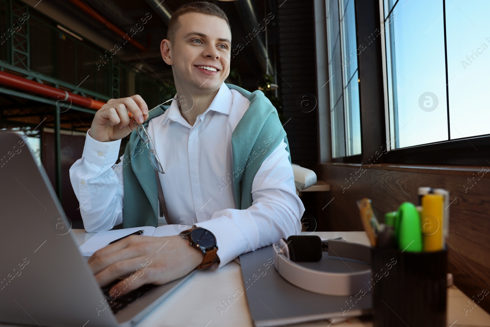 Photo of Young male student with laptop studying at table in cafe, low angle view