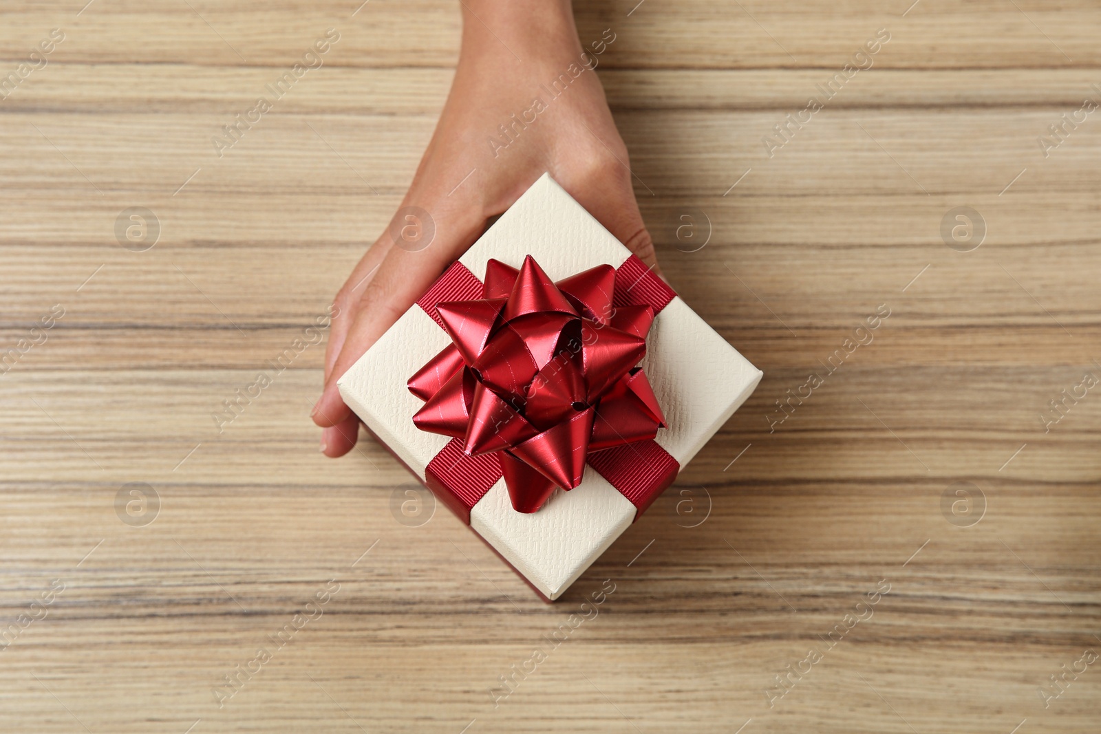 Photo of Woman holding beautiful gift box over wooden table, top view