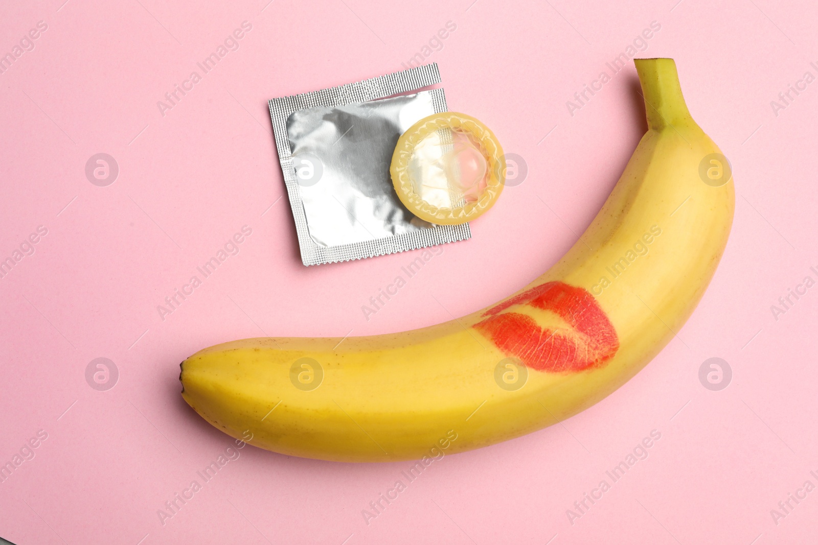 Photo of Condom and banana with lipstick kiss mark on pink background, flat lay. Safe sex