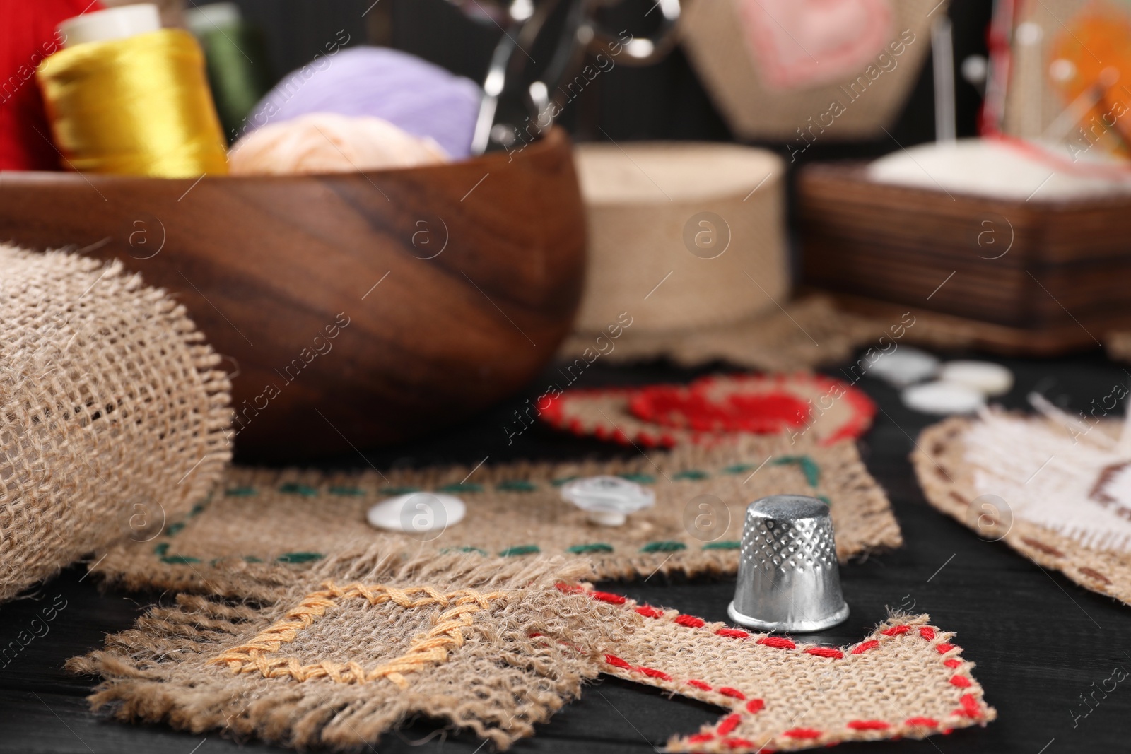 Photo of Pieces of burlap fabric with different stitches and thimble on black table, closeup