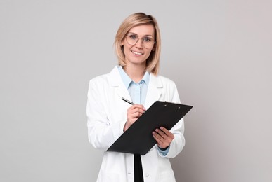 Photo of Smiling doctor with clipboard on grey background
