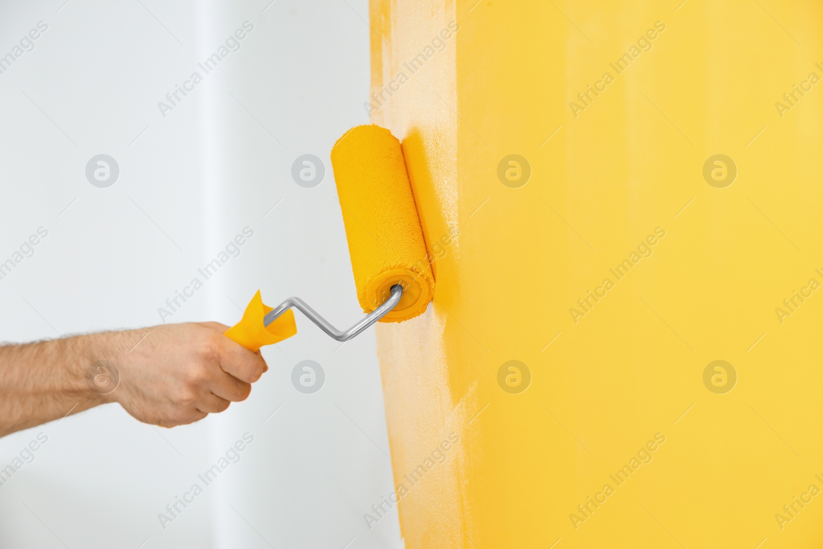 Photo of Man painting white wall with yellow dye, closeup. Interior renovation