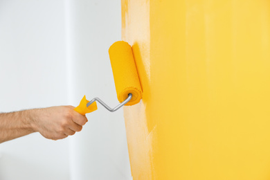 Photo of Man painting white wall with yellow dye, closeup. Interior renovation