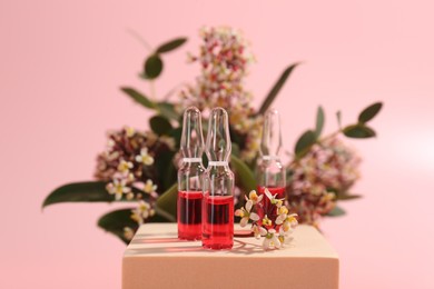 Stylish presentation of skincare ampoules and flowers on pink background, closeup