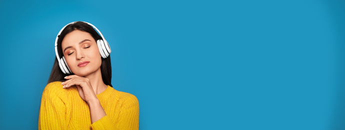 Image of Young woman listening to music with headphones on blue background, space for text. Banner design