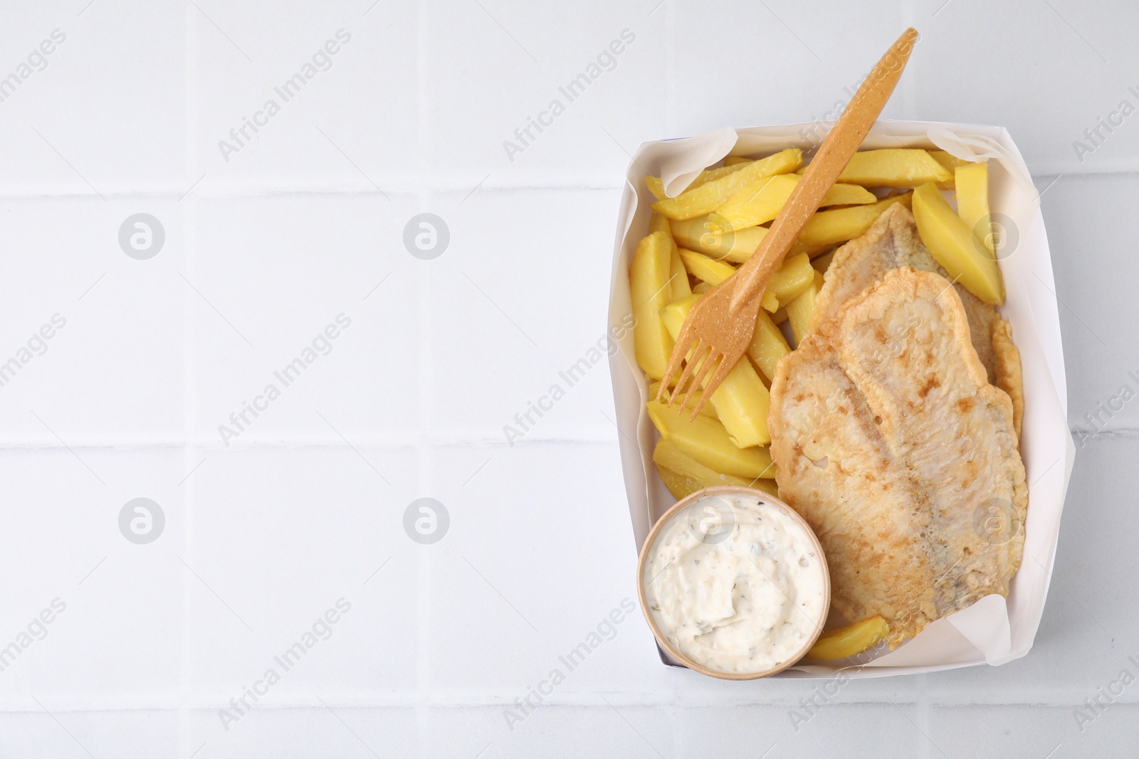 Photo of Delicious fish and chips with tasty sauce served on white tiled table, top view. Space for text