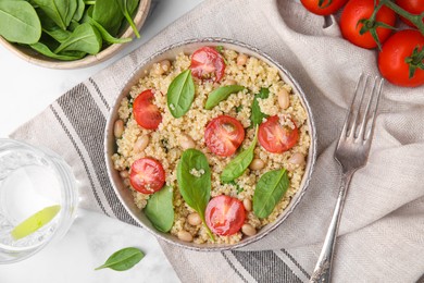 Delicious quinoa salad with tomatoes, beans and spinach leaves served on white table, flat lay