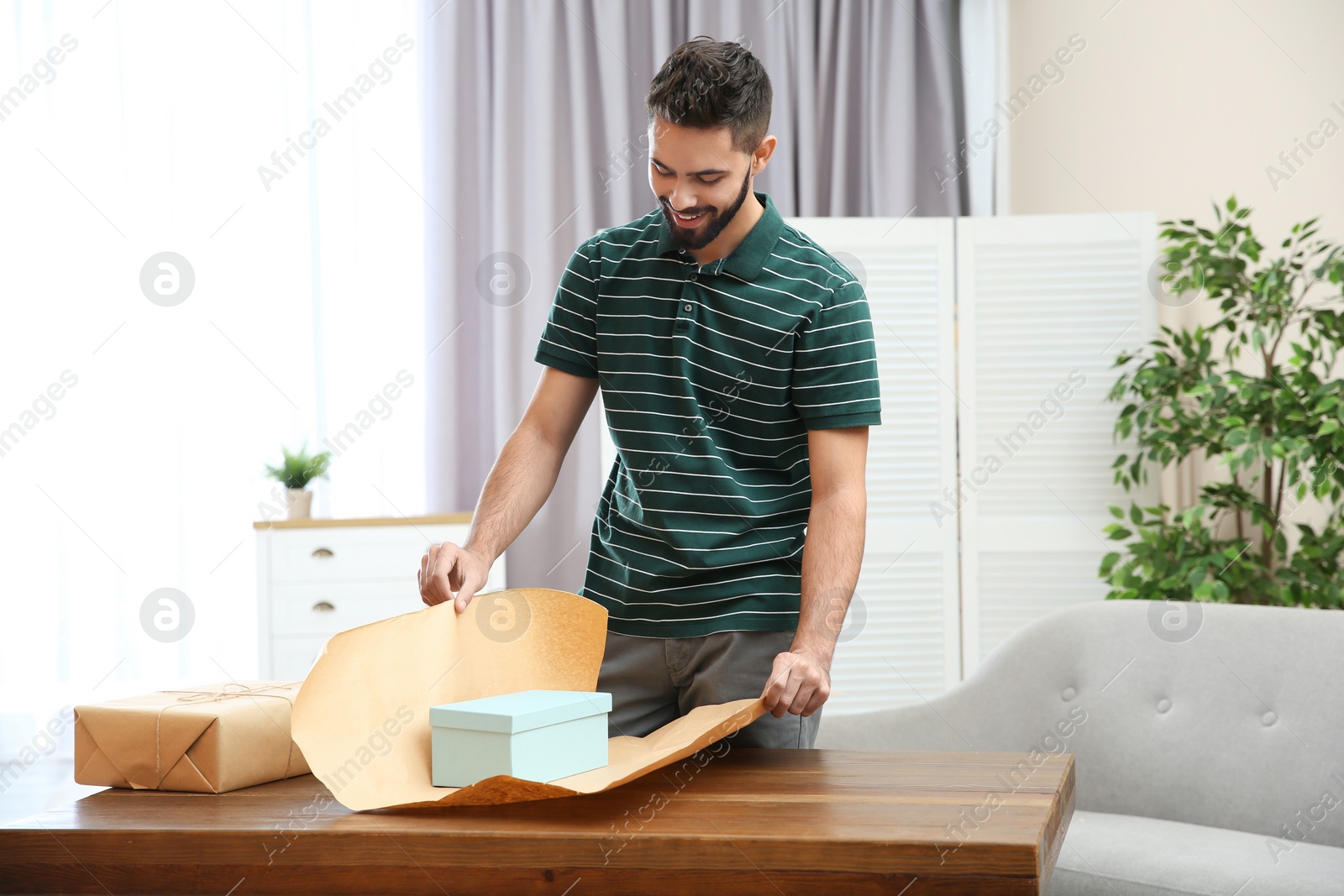 Photo of Young man wrapping parcel on table at home