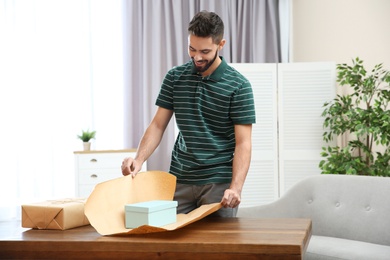 Photo of Young man wrapping parcel on table at home