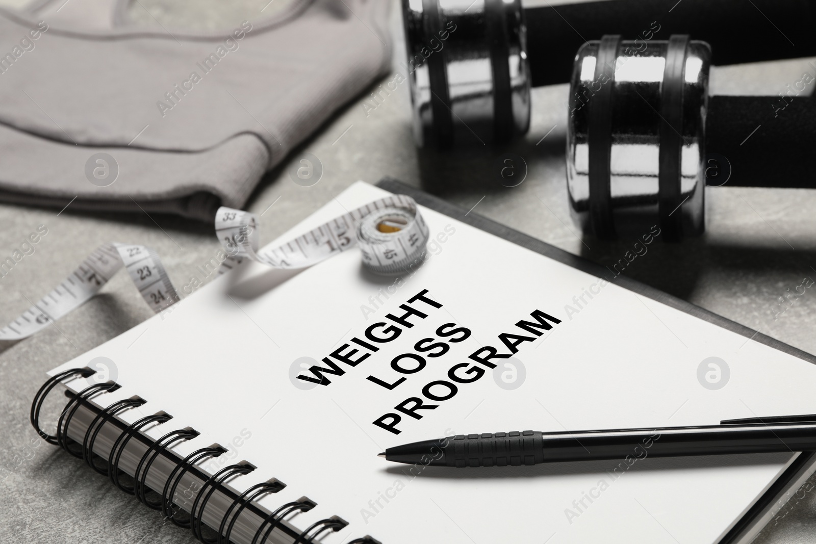 Photo of Weight loss concept. Notebook with pen and measuring tape on grey table, closeup