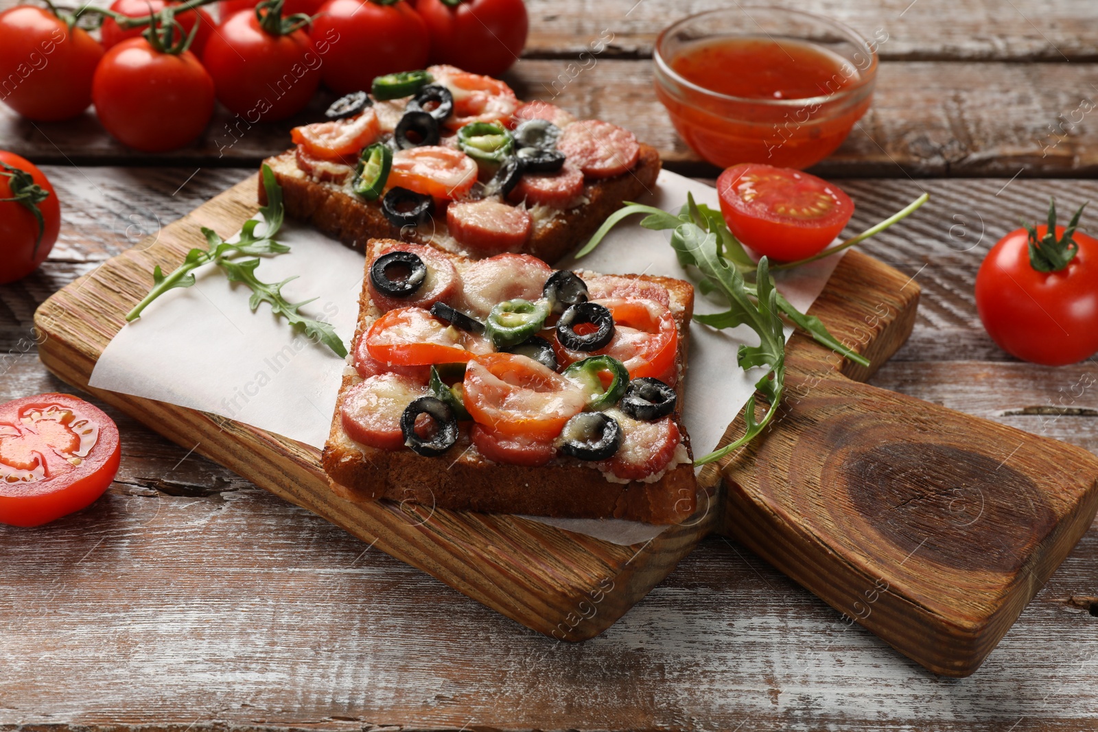 Photo of Tasty pizza toasts, sauce, tomatoes and arugula on wooden table