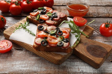 Tasty pizza toasts, sauce, tomatoes and arugula on wooden table