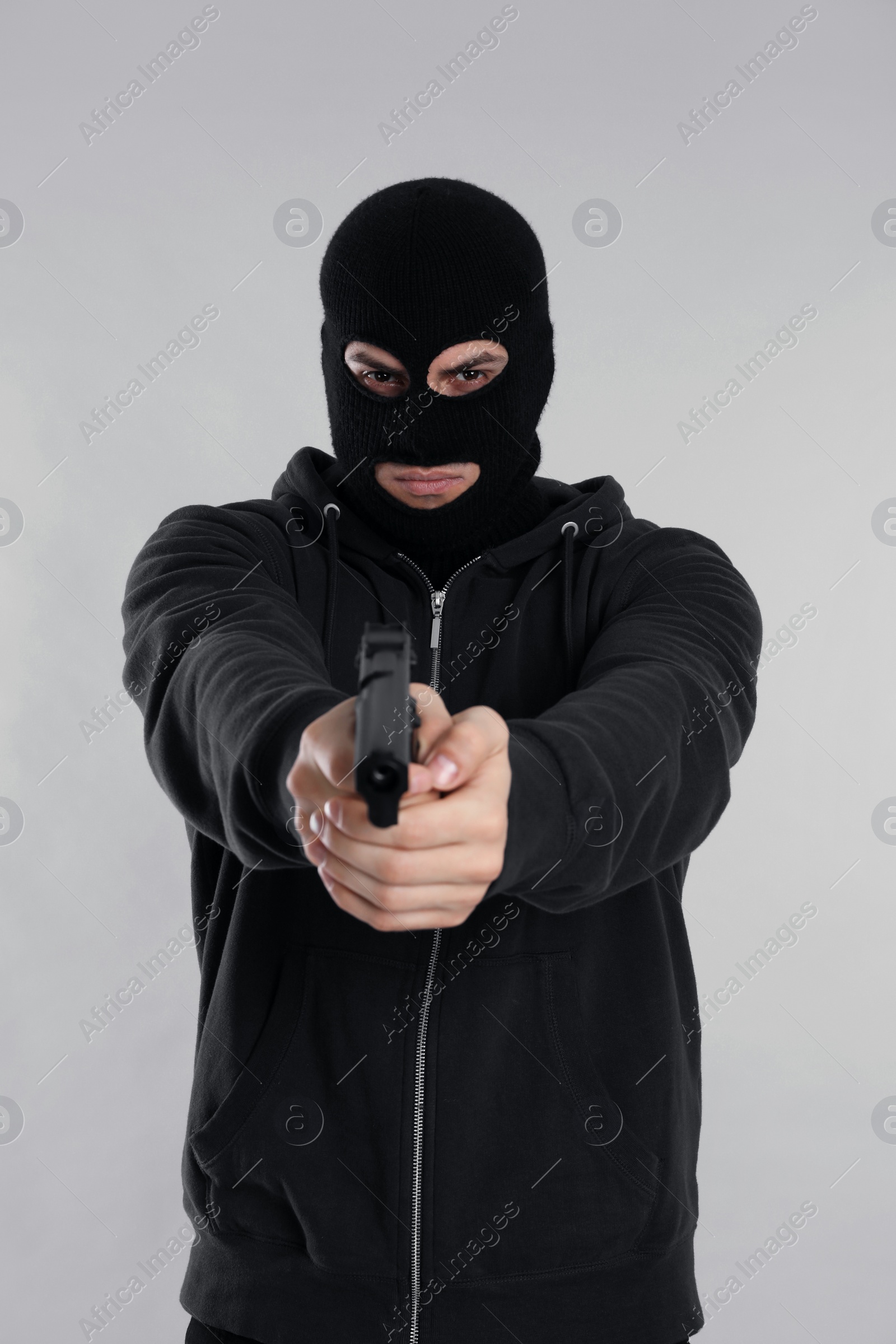 Photo of Man wearing black balaclava with gun on light grey background