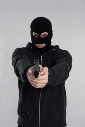 Man wearing black balaclava with gun on light grey background