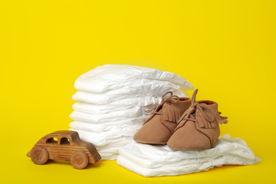 Photo of Diapers, toy car and baby shoes on yellow background
