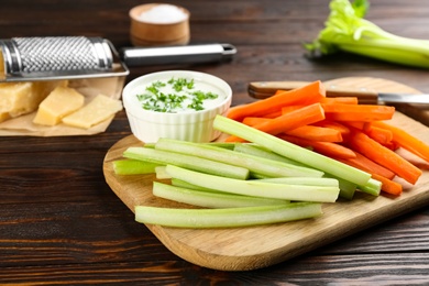 Photo of Celery and carrot sticks with dip sauce on wooden table