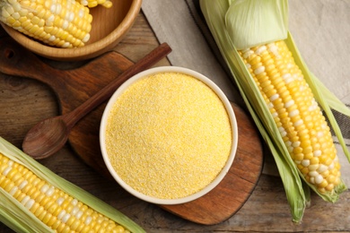 Photo of Cornmeal in bowl and fresh cobs on wooden table, flat lay