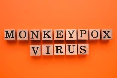 Photo of Words Monkeypox Virus made of wooden cubes on orange background, flat lay