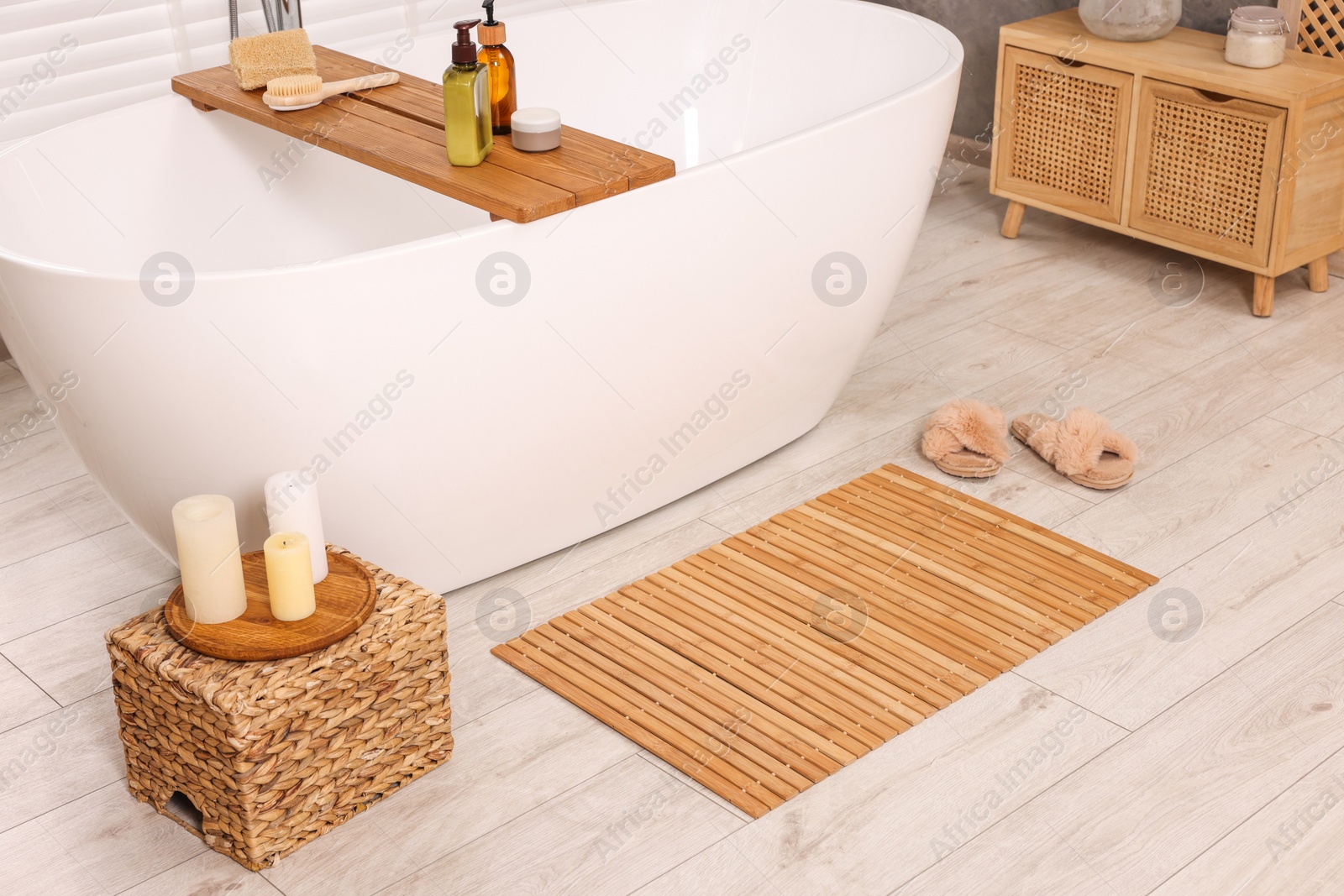 Photo of Stylish bathroom interior with bamboo bath mat and white tub