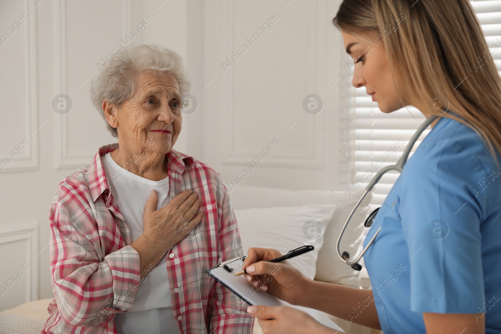 Photo of Young caregiver examining senior woman in room. Home health care service