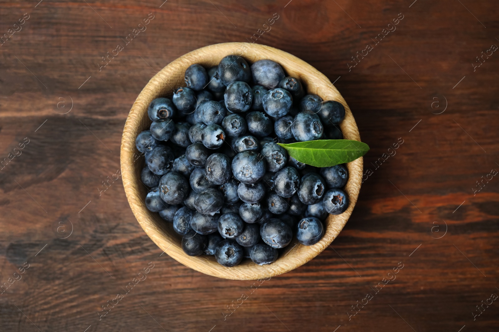 Photo of Tasty ripe blueberries in bowl on wooden table, top view