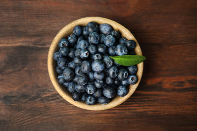 Tasty ripe blueberries in bowl on wooden table, top view