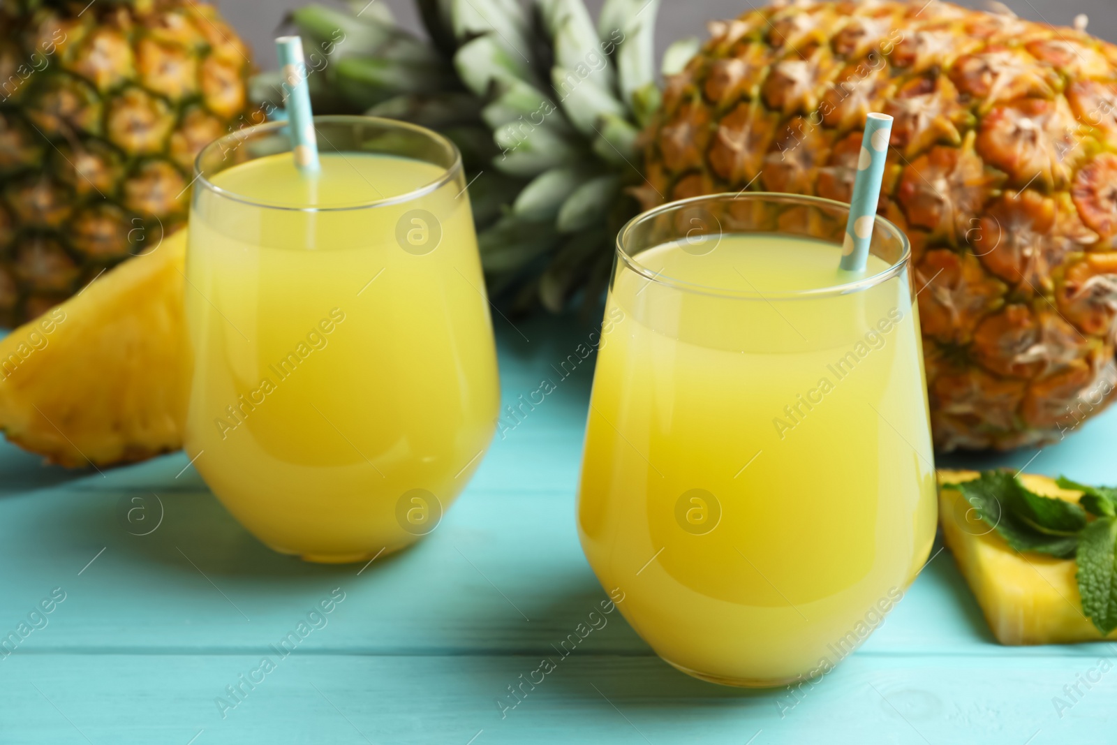 Photo of Delicious fresh pineapple juice on light blue wooden table