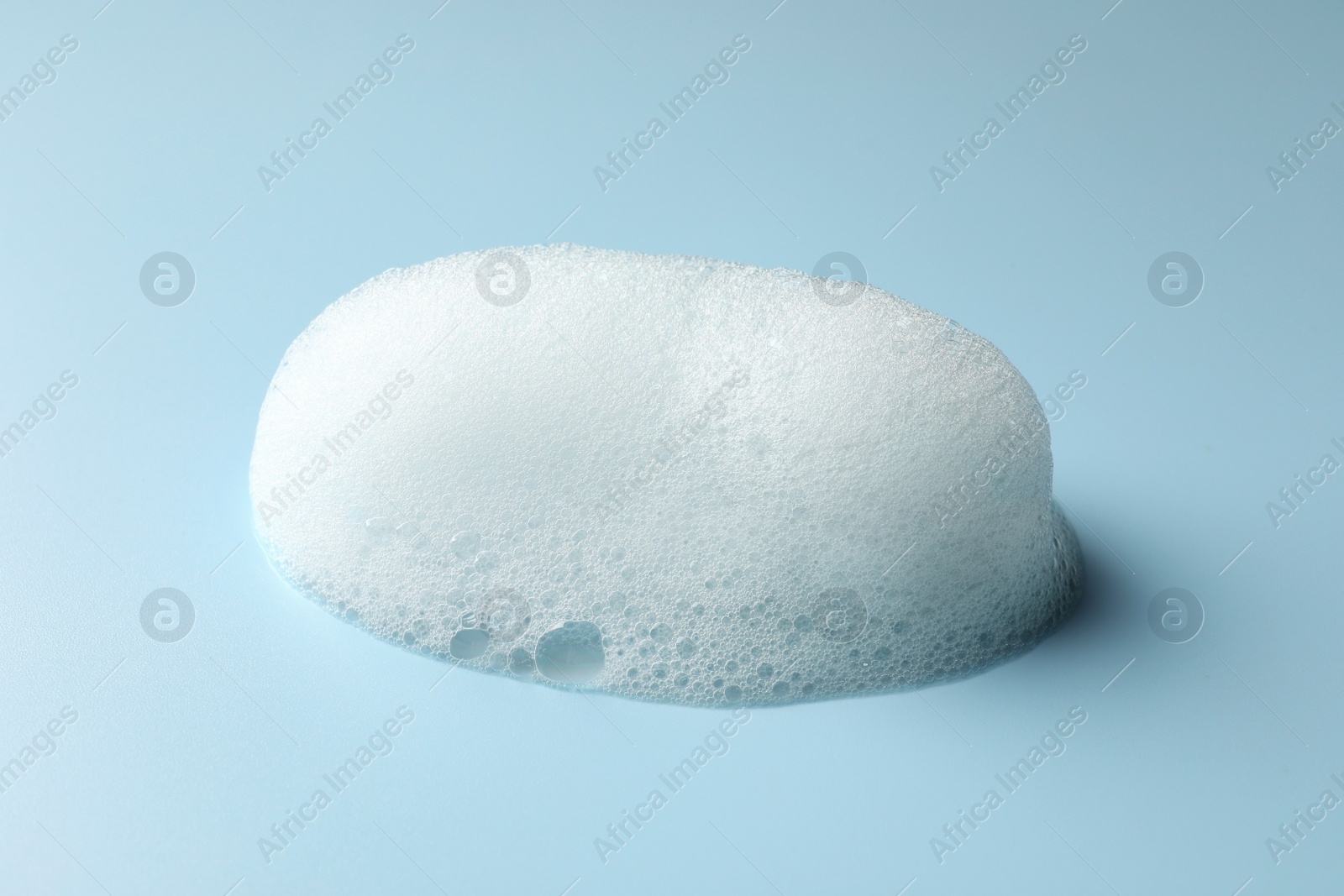 Photo of Drop of fluffy soap foam on light blue background