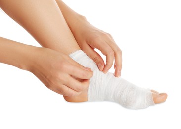 Photo of Woman wrapping foot in medical bandage on white background, closeup