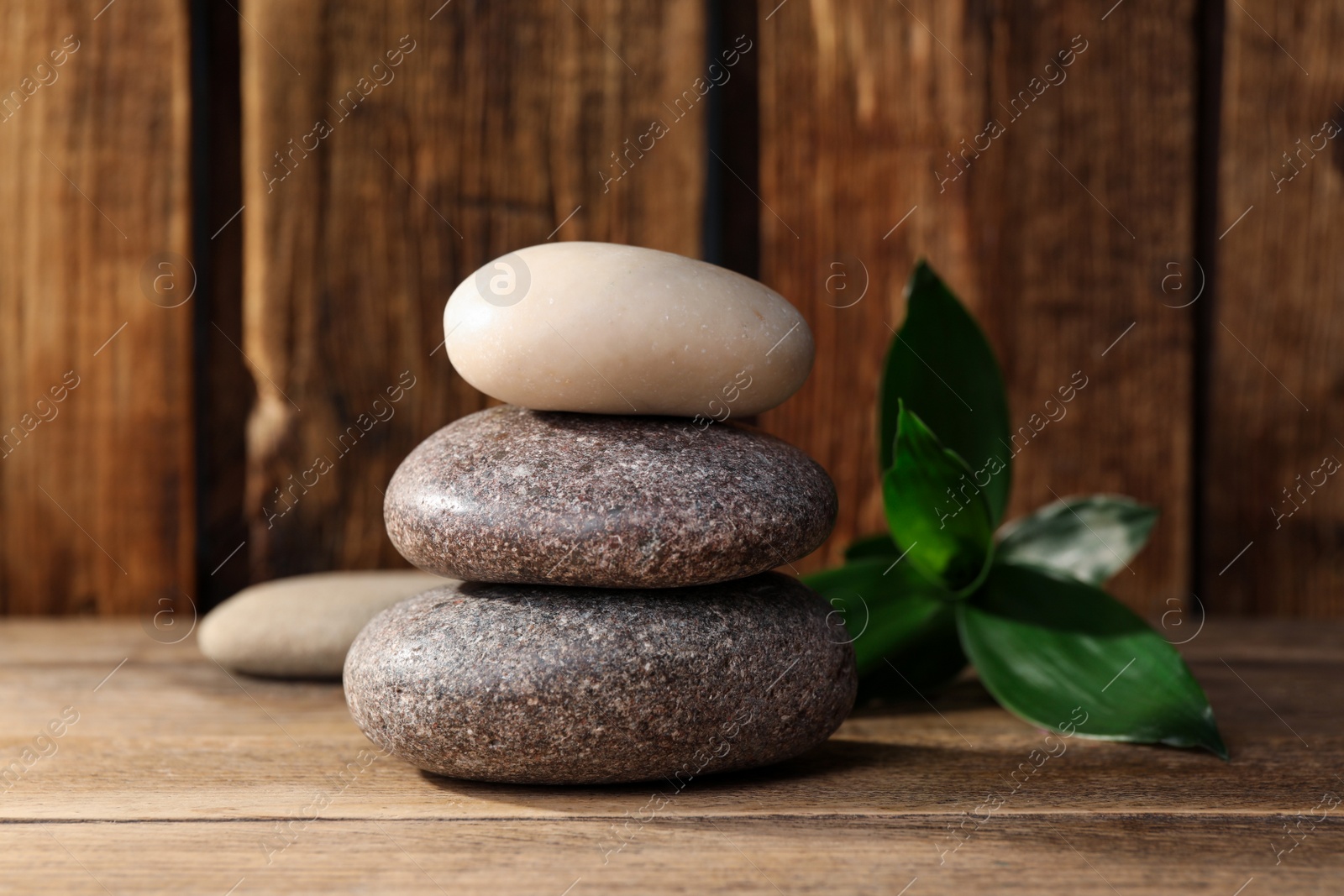 Photo of Stacked spa stones and bamboo leaves on wooden table