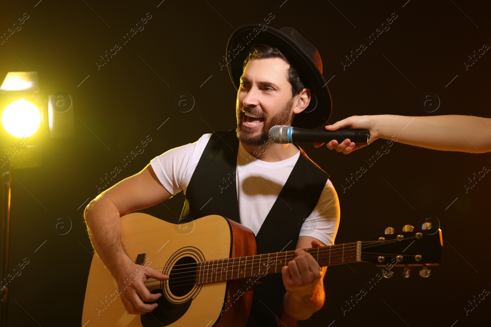 Photo of Handsome man with acoustic guitar singing while woman holding microphone on dark background, closeup