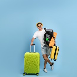 Male tourist with travel backpack and suitcases on turquoise background