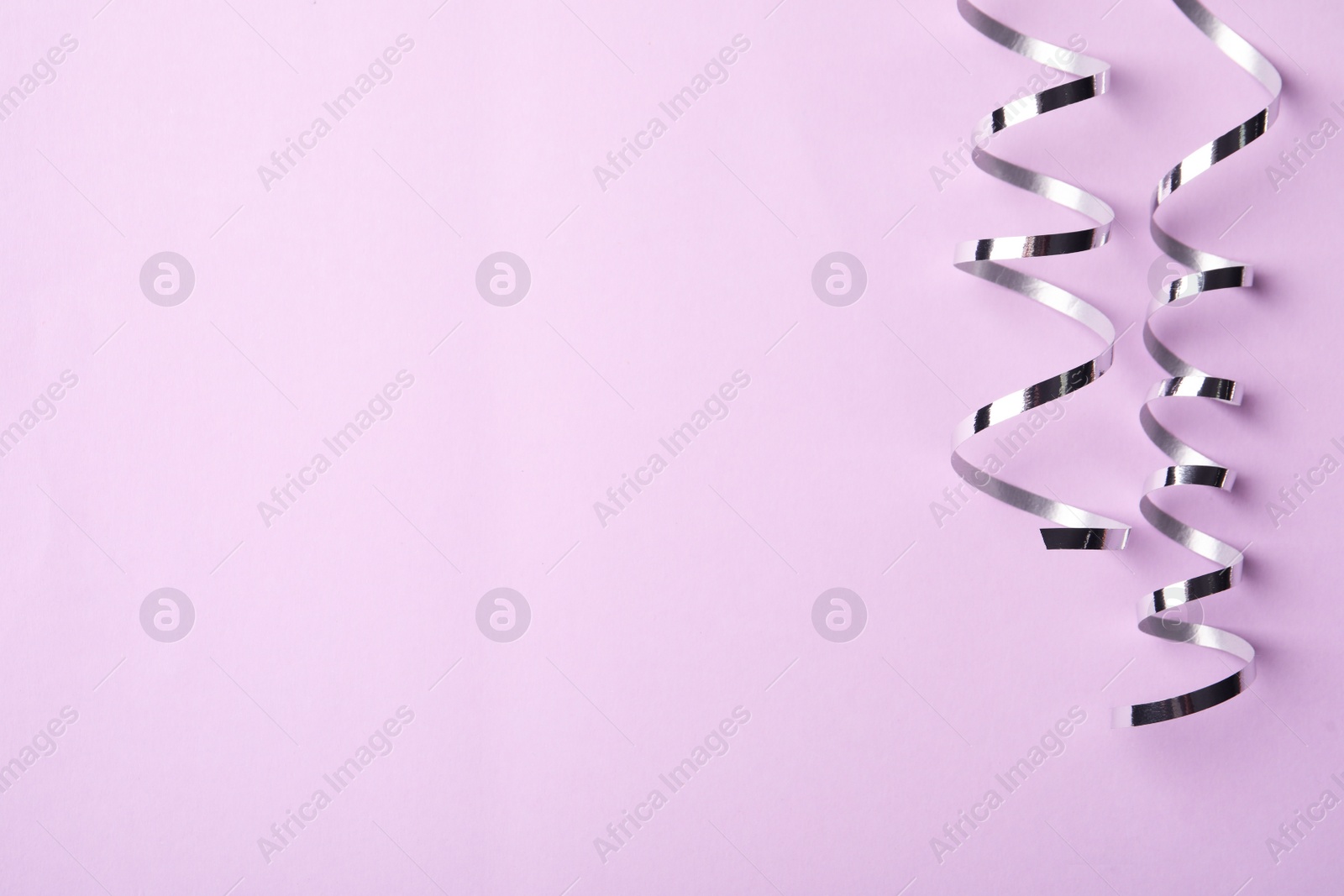 Photo of Shiny silver serpentine streamers on pink background, flat lay. Space for text