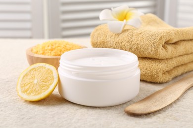 Body care. Composition with moisturizing cream in open jar and half of lemon on light textured table, closeup