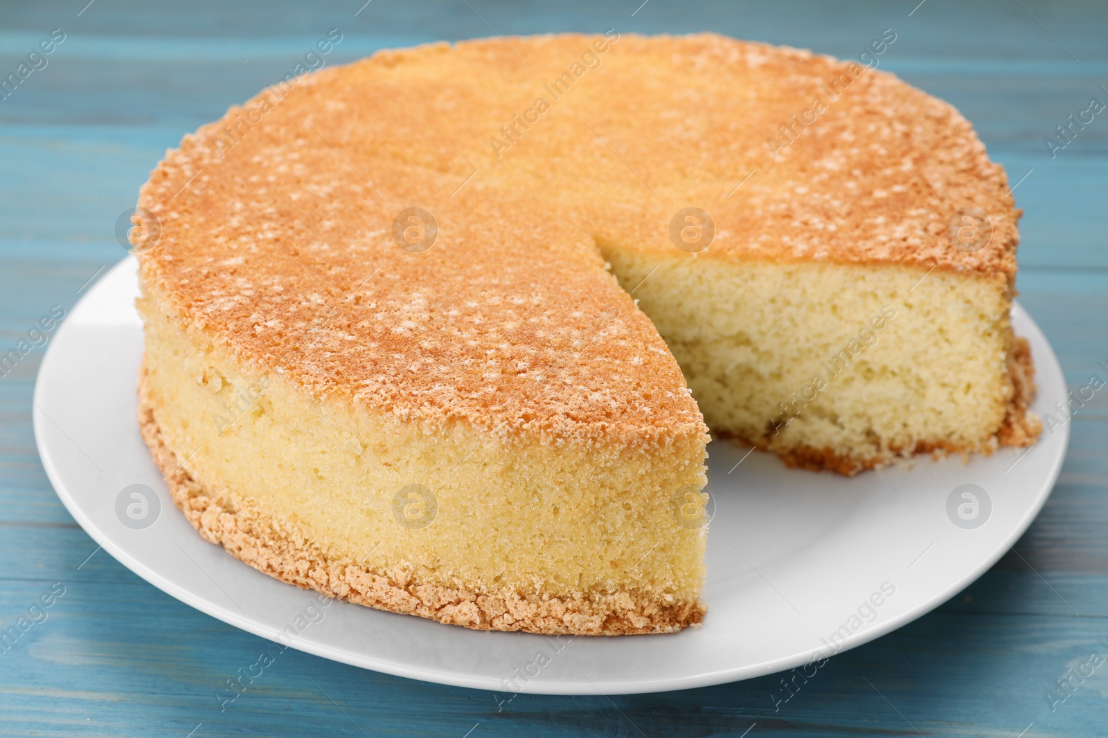 Photo of Plate with cut tasty sponge cake on light blue wooden table, closeup