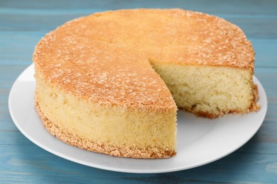 Plate with cut tasty sponge cake on light blue wooden table, closeup