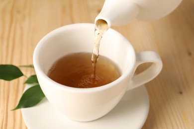 Photo of Pouring tasty tea into cup at light wooden table, closeup