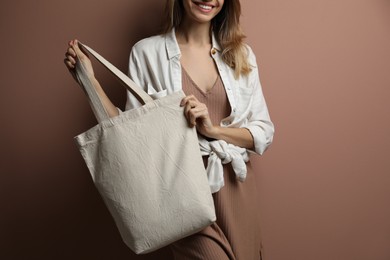 Photo of Happy young woman with blank eco friendly bag against light brown background, closeup