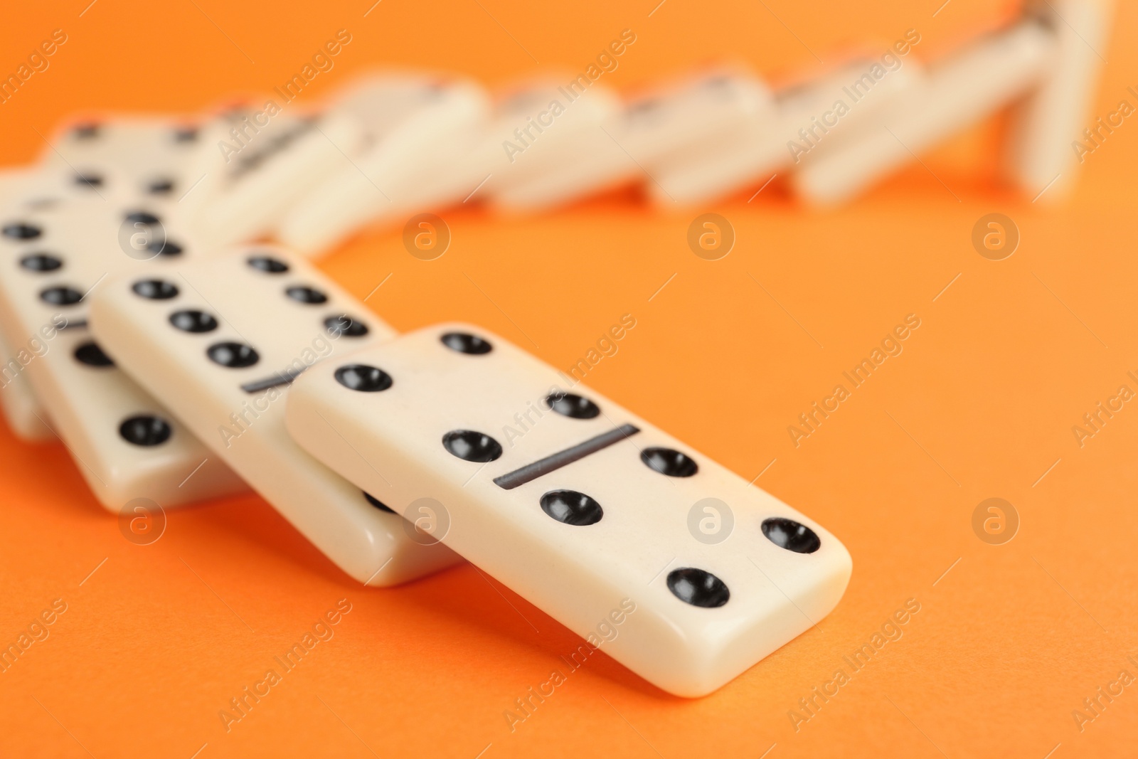 Photo of White domino tiles falling on orange background, closeup